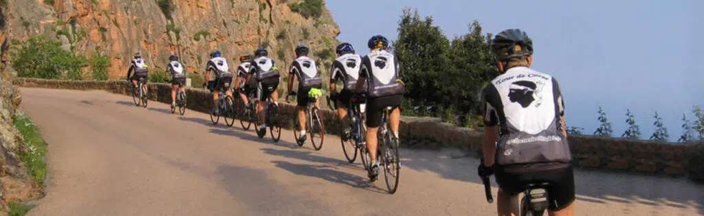 Un groupe de cyclistes avec un maillot "Tour de Corse" qui grimpe un col